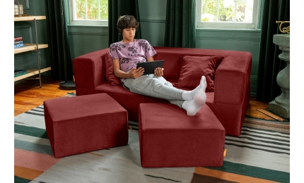 Model sitting on Zipline Convertible Loveseat with pillows and ottomans in Berry